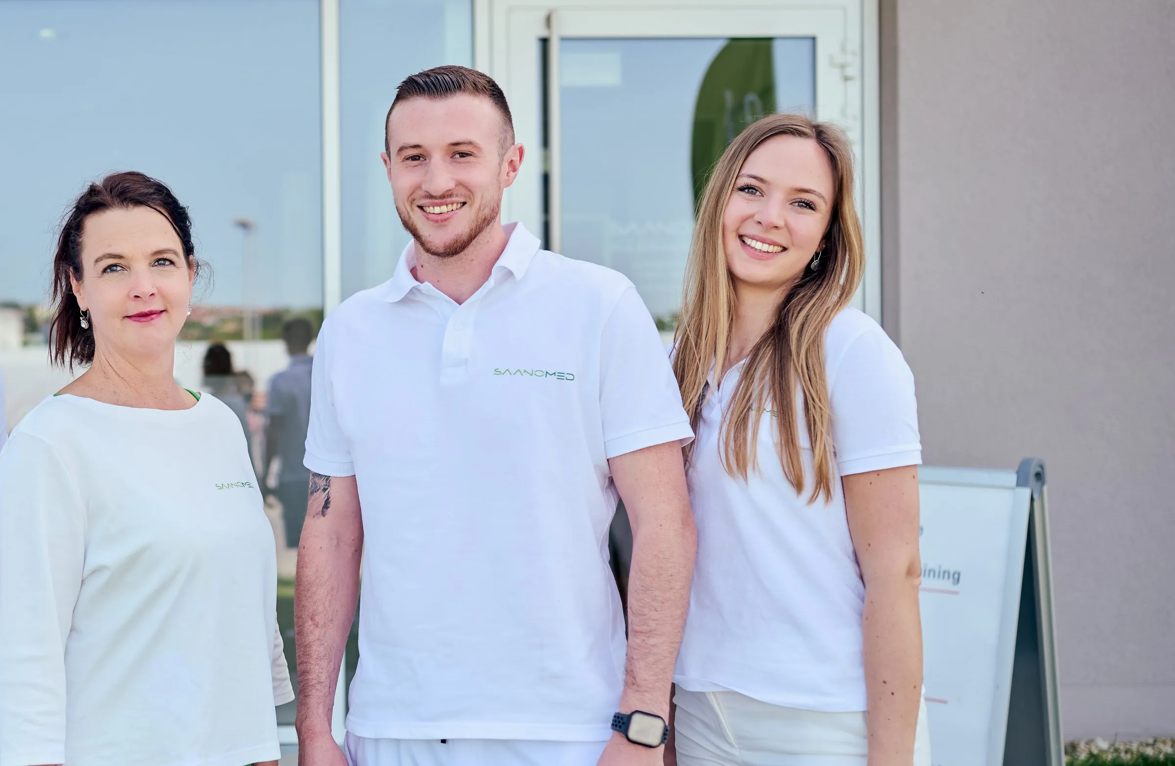 Das Team von SaanoMed in weißen Poloshirts vor dem Eingang der Praxis in Passau
